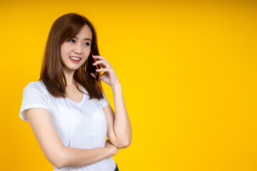 Smiling young Asian woman is pointing on smartphone standing on yellow background.