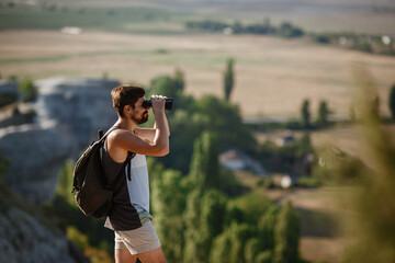 Guy looking at binoculars in hill. man in t-shirt with backpack.