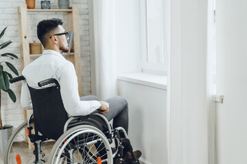 Fototapeta na wymiar Young disabled man sitting in a wheelchair near the window