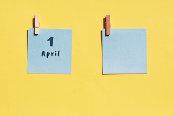 April 1st. Day of 1 month, calendar date. Two blue sheets for writing on a yellow background. Top view, copy space. Spring month, day of the year concept