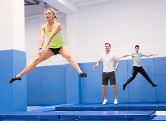 Athletic young woman training jumping movements in indoor trampolines center