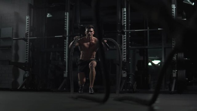 Healthy lifestyle, athletic man performs exercises with battle ropes, endurance training in the gym, 4k slow motion.