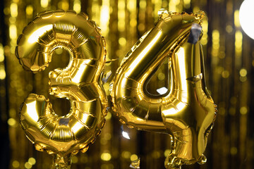 The golden number 34 thirty four is made of an inflatable balloon on a yellow background. One of...