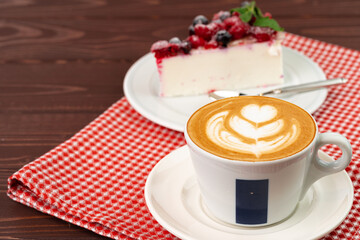 Cup of latte coffee with piece of berry cheesecake