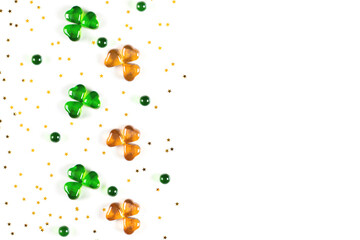 Shamrock symbols made of green and orange glass hearts lying on white background with sparse gold stars confetti. Happy St. Patrick's Day Irish holiday card 17 march lucky clover. Flat lay, copy space