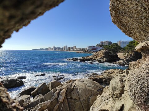 Vista del mar entre rocas desde el camino de ronda de Cala del Pi a Playa de Aro. Al fondo de la imagen Playa de Aro (Costa Brava)