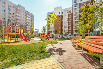 Fototapeta na wymiar New modern green courtyard of city high-rise buildings with children playground, walkways and benches in sunny summer day