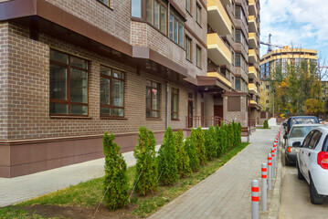 Fototapeta na wymiar Small green lawn with row of thuja trees in courtyard of new modern high-rise residential building. Landscaping in urbanized environment