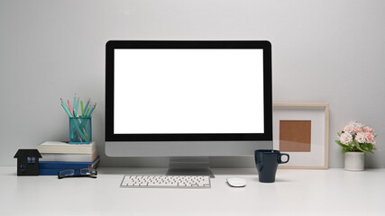 Front view of modern computer with blank screen and office supplies on white office desk.