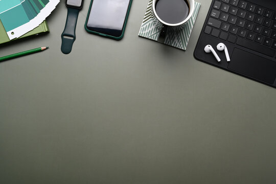 Top view of creative designer workplace with smart watch, mobile phone , wireless keyboard, color swatches, earphone and copy space on green table.