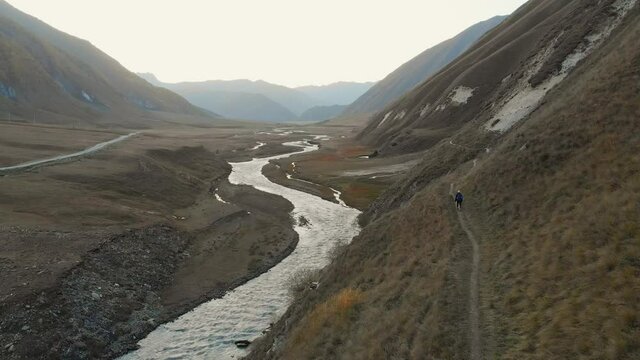 Static aerial view back side one female hiker walking dow path with beautiful landscape background. Kazbegi national park