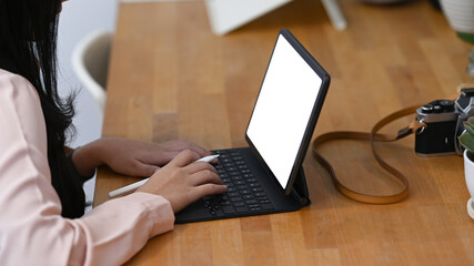 Side view of young female photographer working with tablet computer on wooden table.