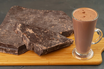 Hot cocoa drink in glass cup and chocolate bar on gray background