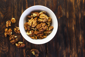 peeled walnuts in the white bowl close on brown old wooden table. healthy food concept