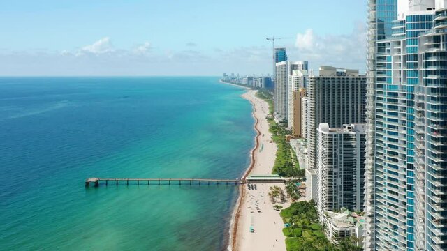 Cinematic aerial Miami beach. Sunny summer day with copy space on blue green background. Travel business footage, drone 4K. Florida vacation USA. Modern water front buildings with beach and ocean view