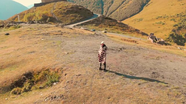 Caucasian woman stands excited in mountains with Kazbegi trinity church in background.Sightseeing and travel in caucasus