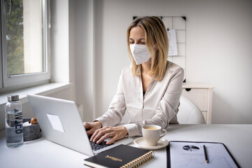 Corona office challenge, business woman wearing ffp2 mask working on laptop in office