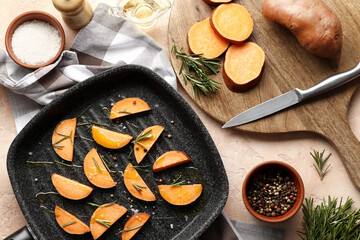 Composition of sliced sweet potatoes in a grill pan, rosemary spice, knife, salt, vegetable oil, kitchen board, top view. Space for text.
