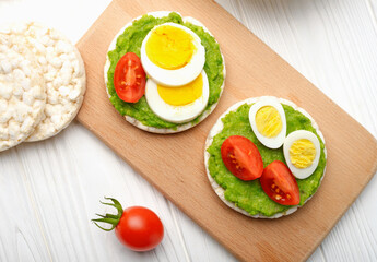 Top view rice cakes with avocado mash and eggs with tomato on cutting board: concept healthy and hearty breakfast