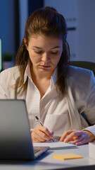 Business woman working overtime to respect deadline of project sitting in business office typing on laptop late at night. Busy focused employee using modern technology network wireless searching