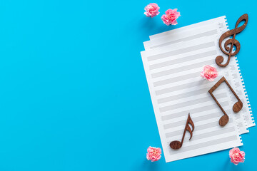 Musical sheet with wooden notes and flowers, top view