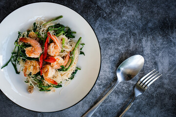 Stir-fried rice vermicelli and water mimosa with prawns on white plate with cutlery.