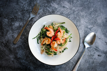 Stir-fried rice vermicelli and water mimosa with prawns on white plate with cutlery.