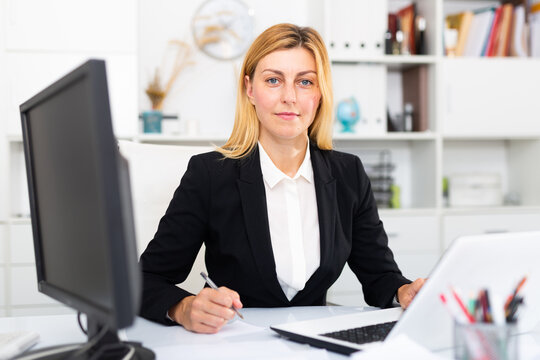 Positive young businesswoman working with laptop and documents in office