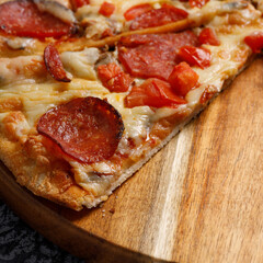 Pepperoni pizza, on a black textured background. Italian food concept. Square. Close-up.
