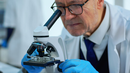 Elderly man in modern equipped lab making research using microscope. Senior scientist working with...