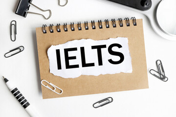 IELTS.text on white paper over white background. notebook, pen.