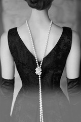 Beautiful female figure from the back in a black dress and pearls in the style of 20-30 years of...