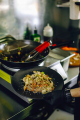 cooking vegan wok noodles with vegetables in cafe kitchen