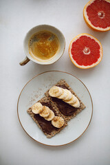 a cup of coffee with milk and crispbreads with chocolate paste and banana pieces