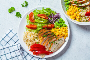 Grilled chicken breast with brown rice and vegetables in white plate, gray background, top view. Healthy food concept.