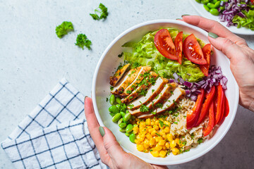 Grilled chicken breast with brown rice and vegetables in white plate, gray background, top view. Healthy food concept.