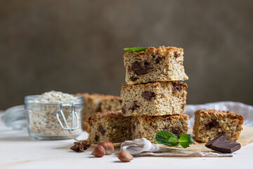 Oatmeal squares with chocolate, nuts, pieces of chocolate and mint, light concrete background. Diet bars. Healthy bakery for breakfast or dessert.