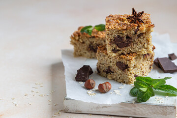 Oatmeal squares with chocolate, nuts, pieces of chocolate and mint, light concrete background. Diet bars. Healthy bakery for breakfast or dessert.