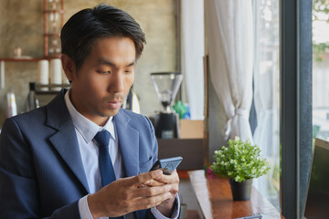 Zoom View Front Right Asian Businessman in Suit Chat Online with Customer by Smartphone in Coffee Shop Scene. Asian Businessman Work from Anywhere with Technology