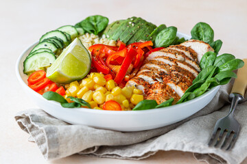 Healthy buddha bowl lunch with grilled chicken and bulgur, spinach, avocado, cucumber, bell pepper and corn on light background. Delicious balanced food concept.