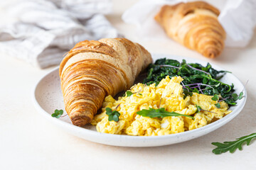 Croissant served with scrambled eggs and spinach on plate, light concrete background. Breakfast.