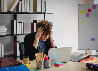 caucasian businessman dressed formally sitting on a desk looking at a laptop on a working table put his hands on his head with serious and unhappy expression. Finacial depression bankrupt concept