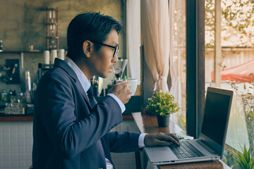 Right Asian Businessman in Suit and Tie Wear Glasses Hold Coffee Cup and Typing Laptop in Coffee Shop Scene. Asian Businessman Work from Anywhere with Technology in Vintage Tone