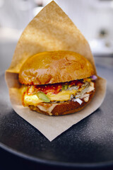 juicy burger in brown paper on a black plate