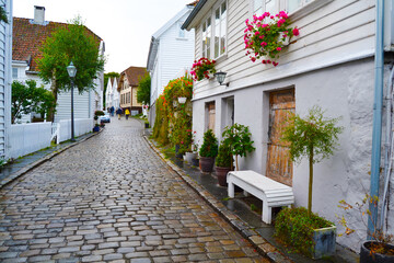 Fototapeta na wymiar White wooden houses decorated with flowers and plants in the historic district Gamle Stavanger (Old Stavanger), Norway. Rainy day in summer season in Stavanger.