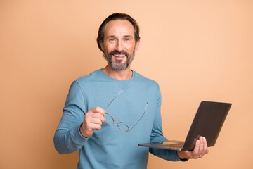 Photo portrait of man taking off glasses holding laptop isolated on pastel beige colored background