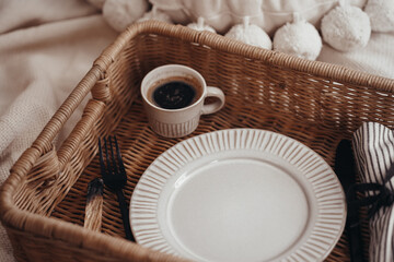 Wooden wicker tray with dishes, plate and coffee cup in boho interior 