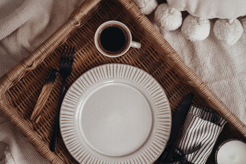 Wooden wicker tray with dishes, plate and coffee cup in boho interior 
