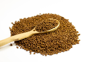 Buckwheat tea in a wooden spoon on a white background. Isolate. Buckwheat tea close-up macro photography. Scattered buckwheat tea pellets on white background.