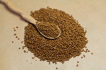 Buckwheat tea in a wooden spoon on a brown background. Buckwheat tea close-up macro photography. Scattered buckwheat tea pellets on brown background.